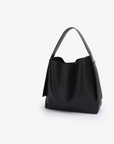 Remi and Reid Paloma Shoulder Bag in textured black vegan leather, featuring a unique wing-like silhouette with a flat top handle and a removable, adjustable shoulder strap.