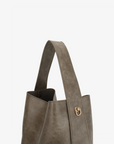 Paloma Waxed vegan leather shoulder bag in gray featuring a wide single strap handle and gold-tone buckle hardware on the side.